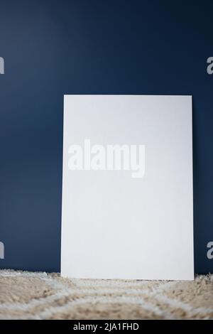 Ein weißes Blatt Papier steht senkrecht auf einem hellen Teppich und einem isolierten dunklen Hintergrund Stockfoto