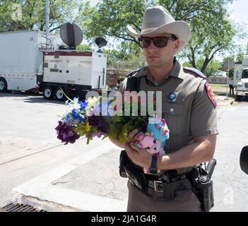 Uvalde, Texas, USA. 25.. Mai 2022. Ein Beamter des Texas Department of Public Safety sammelt Blumen von einem Bewohner von Uvalde vor der Robb-Grundschule im Süden von Uvalde, wo ein einmütiger Schütze 19 Schüler und 2 Lehrer tötete. (Bild: © Bob Daemmrich/ZUMA Press Wire) Stockfoto