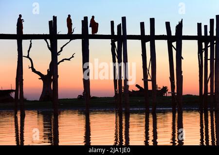 Drei buddhistische Mönche, die in der Dämmerung auf der U-Bein-Brücke in Amarapura, Mandalay, Myanmar, spazieren. Stockfoto