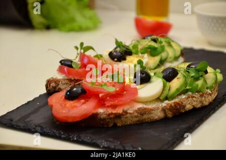 Sandwich mit Avocado, mit Tomaten, Frischkäse, Microgreens und Ei. Vollkornbrot Toast in Scheiben geschnitten Avocado und Ei für ein gesundes Frühstück oder Snack. k Stockfoto