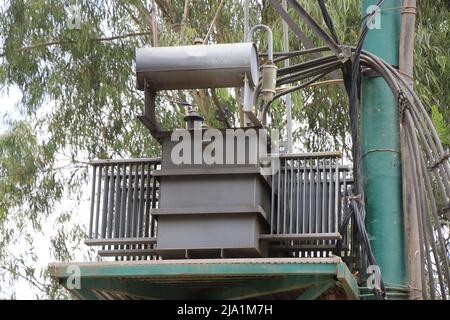 Transformator auf einem Metallmast. Dreiphasige Transformatoren und Flöße auf Schienen für die industrielle Hochspannungsversorgung Stockfoto