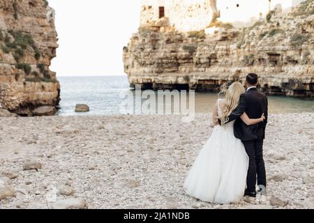 Rückansicht verheiratetes romantisches Paar in Hochzeitskleid und Anzug stehen am Strand, kontemplativ. Vacaion und Feiertagsveranstaltung Stockfoto