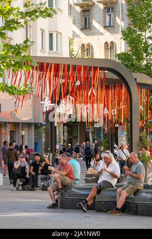 Menschen, die das schöne Wetter auf dem Slaveykov-Platz mit einer bunten Kunstinstallation aus mehreren Genres in Sofia, Bulgarien, genießen Stockfoto