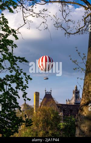 Heißluftballon schwebt über Häusern, eingerahmt von Baumzweigen in Budapest Városliget Stockfoto