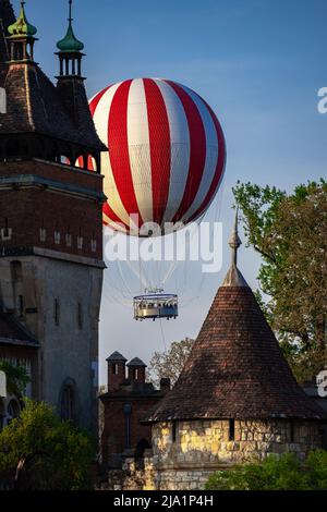 Gestreifter Heißluftballon, der hinter der Burg Vajdahunyad in Budapest Városliget fliegt Stockfoto
