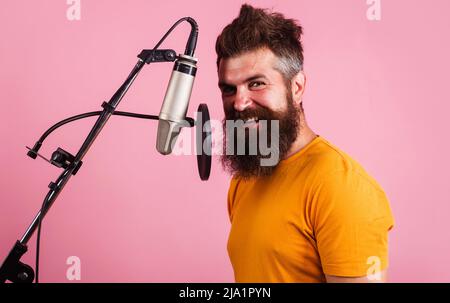 Professioneller Sänger, der im Kondensatormikrofon singt. Lächelnder bärtiger Mann singt in Karaoke. Stockfoto