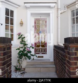 Hauseingang mit rosa, blau und gelb gefärbter Glastür und rosa Blumen draußen, direkt an der Kings Road in Chelsea, London. Stockfoto