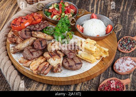 Türkische Küche, gemischter Kebab. Fleischplatte auf Holzkohle gebraten mit Gewürzen auf einem Holzbrett. Lammkarree, Lamm, Kebab, Huhn, Pilze und Tomaten Stockfoto