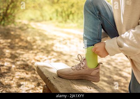 Das Kind schnürt seine Sneakers im Frühlingspark für einen Spaziergang. Mädchen Krawatten Bogen auf ihrem Schuh im Freien. Gesundheits- und Sportkonzept. Hochwertige Fotos Stockfoto