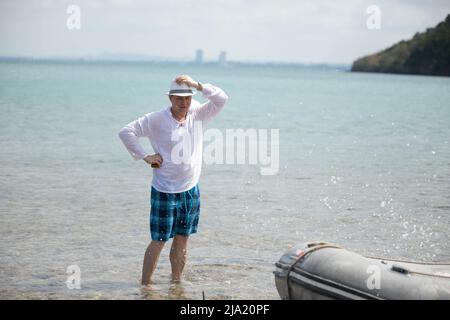 Modischer Mann auf dem Hintergrund der Meereswellen. Seitenansicht, Nahaufnahme. Konzept von Freizeit und Reisen Stockfoto