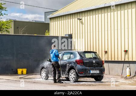 Mann, der in Irland ein Auto bei einer gewerblichen Autowäsche mit einem Hochdruckwasserschlauch wäscht. Stockfoto