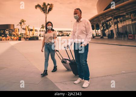 Ein paar Freunde in Schutzmasken plaudern, während sie den Flughafen mit ihrem Gepäck verlassen Stockfoto