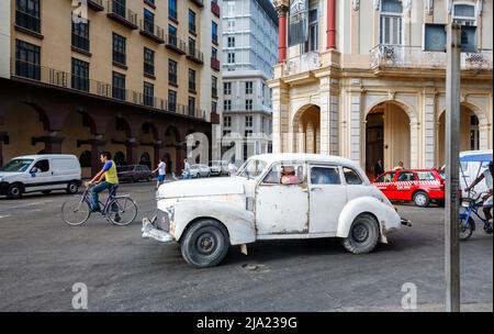 In den Straßen der Innenstadt von Havanna, der Hauptstadt Kubas - typische Straßenszene - wird ein beschädigtes, verrosttes weißes Oldtimer-Auto gefahren Stockfoto