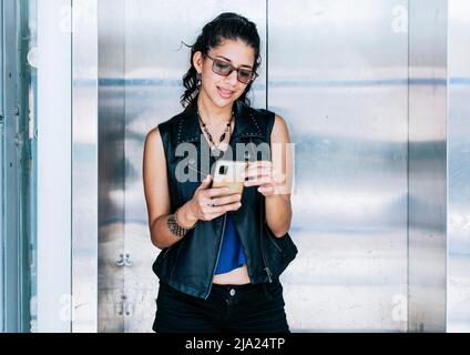 Attraktives Mädchen, das ihr Handy an der Aufzugstür benutzt, eine Person, die im Aufzug SMS schreibt, Nahaufnahme eines städtischen Mädchens, das ihr Handy überprüft Stockfoto