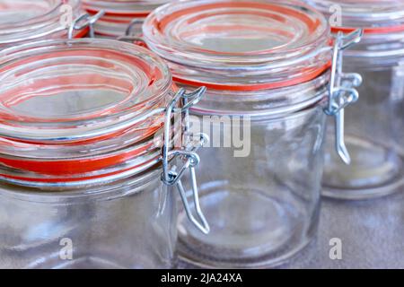 Nahaufnahme von leeren Gläsern oder Konservierbehältern mit orangefarbenem Verschlussring in einer Reihe. Konzept zur Erhaltung von Lebensmitteln. Stockfoto