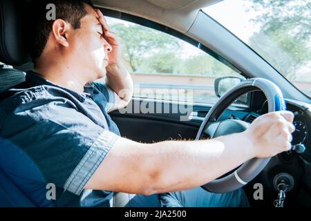 Ermüdete Fahrer stecken im Verkehr, Konzept eines ermüdeten Mannes in seinem Auto, betont. Ein Fahrer mit Kopfschmerzen im Straßenverkehr, Eine Person mit Kopfschmerzen Stockfoto