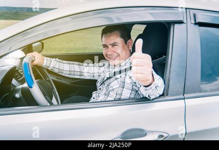 Glücklicher Mann in seinem Auto, der Daumen nach oben zeigt, Porträt eines Mannes, der Daumen nach oben zeigt, während er fährt, Mann in seinem Auto, der Daumen nach oben zeigt Stockfoto