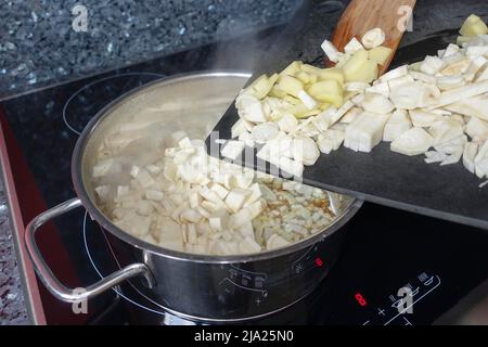 Schwäbische Küche, Vorbereitung Petersilienwurzel (Petroselinum crispum subsp. Tuberosum) wird in Kochtopf, Holzschaber, Induktionsherd, Winter gefüllt Stockfoto