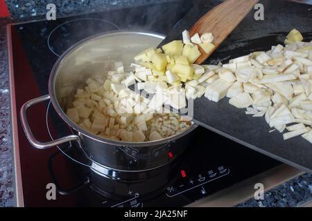 Schwäbische Küche, Vorbereitung Petersilienwurzel (Petroselinum crispum subsp. Tuberosum) wird in Kochtopf, Holzschaber, Induktionsherd, Winter gefüllt Stockfoto