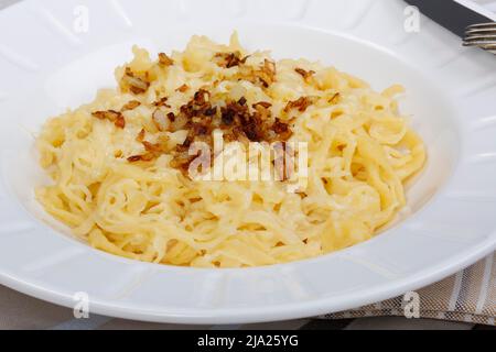 Schwäbische Küche, Kaesspätzle mit geräucherten Zwiebeln, Kaespatzen auf einem Teller, handgeschabter Spätzle, Silberbesteck, Messer, Gabel, Traditionell Stockfoto