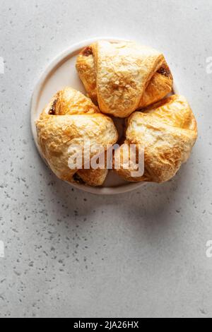 Drei frische Croissants auf einem weißen Teller auf hellem Hintergrund. Speicherplatz kopieren. Flach liegend, Draufsicht Stockfoto