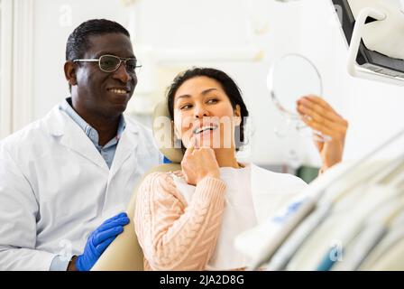 Lächelnde Patientin mit Zahnarzt, der nach Zahnbehandlungen in den Spiegel schaut Stockfoto