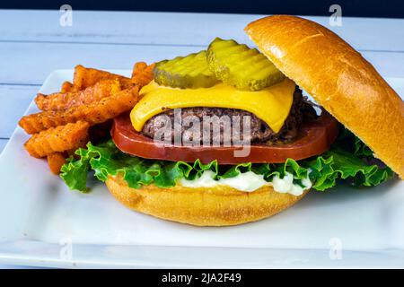 Käseburger auf einem Brioche-Brötchen und serviert mit Süßkartoffelfritten Stockfoto