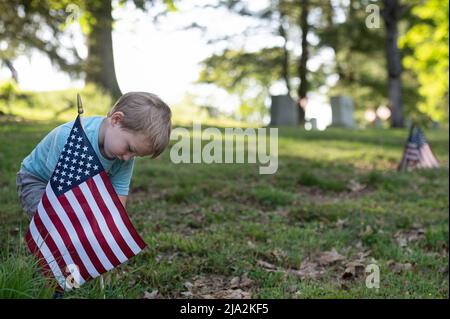 Dallas, Usa. 25.. Mai 2022. Ein kleiner Junge setzt eine Flagge am Grab eines Veteranen des Zweiten Weltkriegs. Mitglieder der American Legion, Boy Scouts und Girl Scouts haben in Vorbereitung auf den Memorial Day-Feiertag zerfetzte Flaggen auf Friedhofs ersetzt. Kredit: SOPA Images Limited/Alamy Live Nachrichten Stockfoto