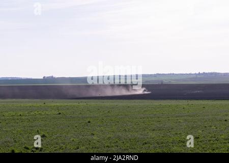 Ein landwirtschaftliches Feld, auf dem ein Traktor mit Pflügen den Boden pflügt, den Boden verarbeitet und für die Aussaat mit einer neuen Ernte vorbereitet Stockfoto