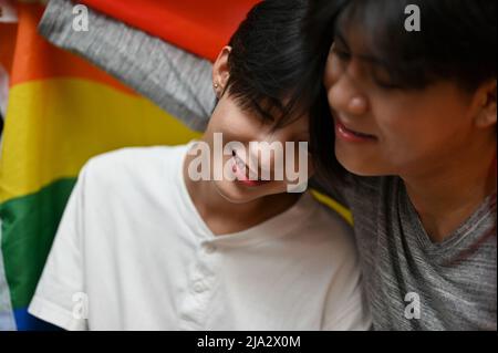 Schöner junger schwuler Mann aus Asien in einer warmen Umarmung seines schwulen Freundes und der LGBT-Flagge. Kuscheln oder Umarmen. Junge LGBT-Paare. Stockfoto