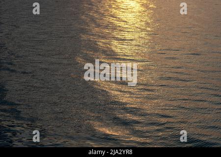 Wunderschöne Sonnenuntergangsreflexion funkelt auf winzigen Wellen der Meereswasserwelle im Hintergrund, Draufsicht. Die Textur des Meerwassers. Stockfoto