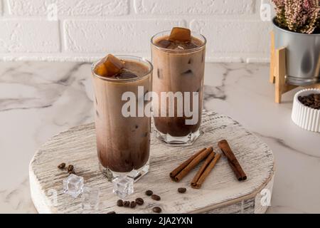 Zwei große Gläser mit Dalgon-Eiskaffee und Kaffeeeiswürfeln auf einem weißen Holzpodest und einem Marmortisch Stockfoto