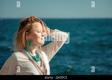 Frau in böhmischer Kleidung am Strand bei Sonnenuntergang. Boho-Stil für modischen Look im Resort. Frau mittleren Alters gut aussehende Frau in weißem Kleid und Boho-Stil Stockfoto