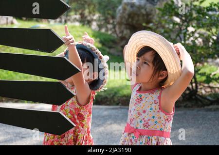Kinder schauen auf Schilder mit Pfeilen, die auf verschiedene Orte im Park zeigen, um eine Wegbeschreibung zum Spielplatz zu finden. Stockfoto