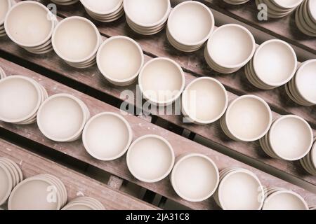 Viele kleine runde Teller aus Keramik-Ton. Keramikbecher in Rack Vorbereitung für Malerei Design auf der Oberfläche in Töpferei. Handwerk und kleinen Bus Stockfoto