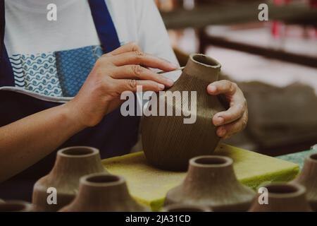 Nahaufnahme der Hand einer Frau, die in einer Töpferwerkstatt Muster auf einer Tonvase macht. Prozess der Herstellung einer Keramikvase. Handwerk und kleine Unternehmen conce Stockfoto