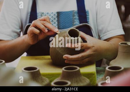 Nahaufnahme der Hand einer Frau, die in einer Töpferwerkstatt Muster auf einer Tonvase macht. Prozess der Herstellung einer Keramikvase. Handwerk und kleine Unternehmen conce Stockfoto