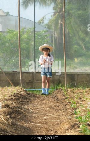 Kleines Mädchen mit Hut hilft ihrer Mutter im Garten, einer kleinen Gärtnerin. Nettes Mädchen spielt im Gemüsegarten. Stockfoto