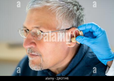 Nahaufnahme der Arzt das Hörgerät im Ohr des älteren Patienten Stockfoto