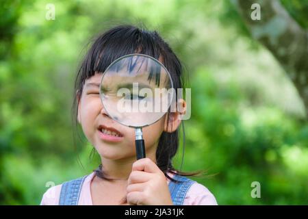 Nettes kleines Mädchen lernen und die Natur mit Outdoor-Lupe erkunden. Neugieriges Kind schaut durch eine Lupe auf einen Baum im Park. Li Stockfoto