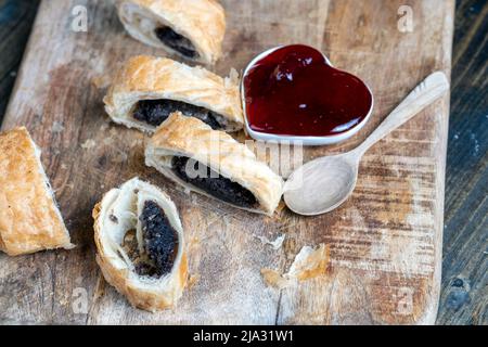 Blätterteig-Brötchen aus Weizenteig und Mohnsaatfüllung, ein Brötchen mit süßer Mohnsaatfüllung auf dem Tisch Stockfoto