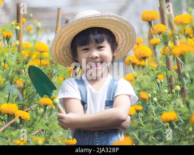 Nettes kleines Mädchen in Hut hält Garten Werkzeug Schaufel für das Pflanzen von Blumen im Garten. Ein Kind hilft Mama im Garten, ein kleiner Gärtner. Stockfoto