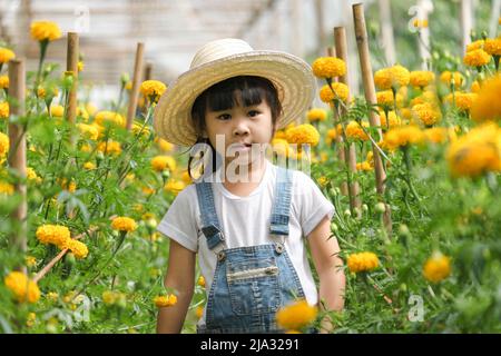 Ein kleines Mädchen mit Hut hilft ihrer Mutter im Ringelgarten, einer kleinen Gärtnerin. Nettes Mädchen spielt in einem schönen Blumengarten. Stockfoto