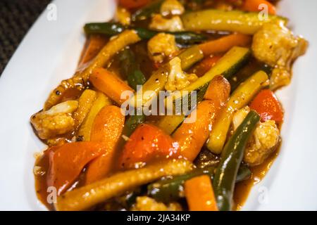 Sautes exotisches Gemüse - Zucchini, Babykorn, Broccoli, Bohnen, Karotten, Pilze, Blumenkohl und Paprika in schwarzer Pfeffersauce gemischt. Stockfoto