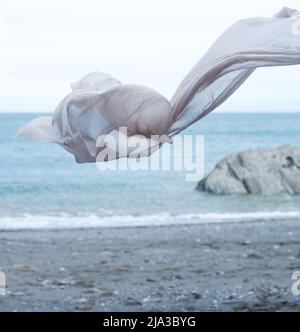Cremefarbener Leinenstoff, der an der Küste im Wind weht. Stockfoto