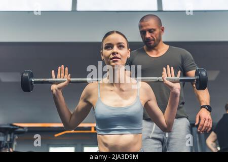 Indoor Gym Portrait einer fokussierten selbstbewussten Brünette in einem grauen Sport-BH mit Langhantel und genieße ihre Zeit im Fitnessstudio. Hochwertige Fotos Stockfoto