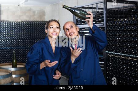 Männer und Frauen, die im Weinkeller stehen und dabei den Sekt in der Flasche betrachten Stockfoto