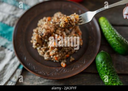 Buchweizenbrei auf der Gabel, den Teller Buchweizenbrei mit den Karotten und dem Fleisch aus der Nähe. Gabel, Gurke, Tomate Stockfoto