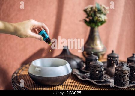 Frau, die ätherisches Öl in den Duftdiffusor auf dem Tisch gegeben hat Stockfoto