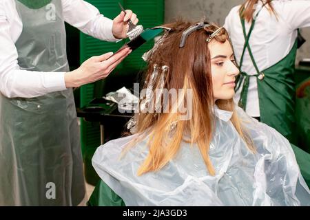 Eine Friseurin färbt das Haar einer jungen kaukasischen Frau in einem Schönheitssalon mit einem Pinsel und einer Folie ein Stockfoto